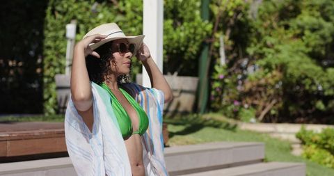 African american woman adjusting straw hat and sunglasses on sunny resort pool steps chic