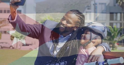 Father taking selfie with child on park bench wearing bike helmet and smiling together