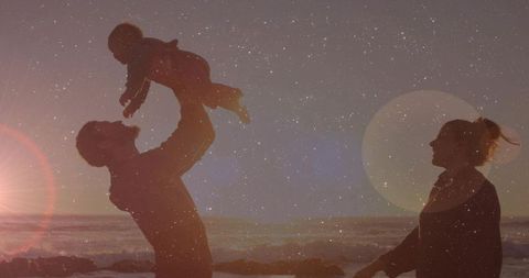 Father lifting baby at golden sunset on rocky beach silhouette with lens flare