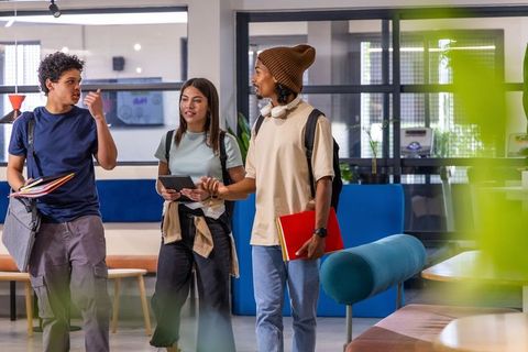 Students walking and talking in modern campus lounge carrying backpacks, books, tablet