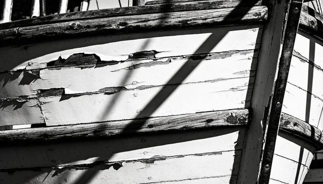 Weathered wooden boat hull showing peeling paint and dramatic shadow lines