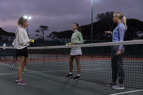 Women tennis players meeting at net during twilight practice under floodlights