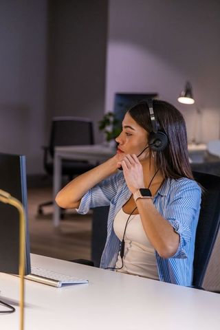 Young woman adjusting headset while working at desktop in modern open-plan office