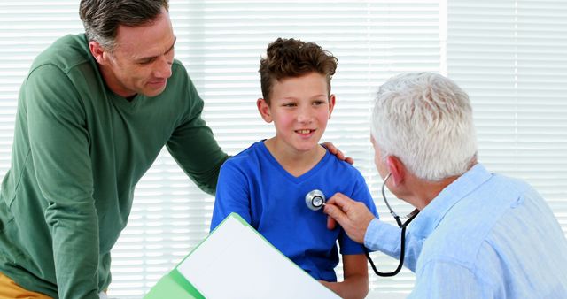 Doctor examines smiling young boy with stethoscope during medical check-up while supportive parent is standing beside. Perfect for healthcare, medical, pediatrician, and family support-related content.