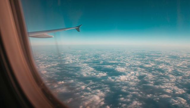 Airplane wing soaring above cloudscape with teal sky and wide horizon