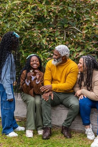 African american multigenerational family laughing and sharing flower in lush garden bench