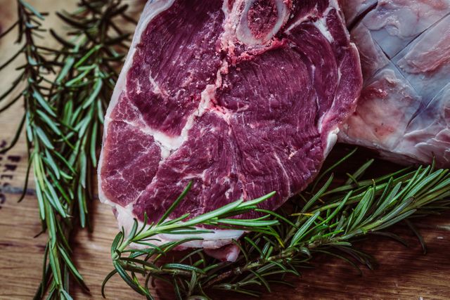 Fresh beef steak lies on wooden surface, accompanied by sprigs of rosemary. Scene emphasizes readiness for culinary preparation, suitable for cooking blogs, restaurant menus, food advertisements, and nutrition articles highlighting protein and meat benefits.