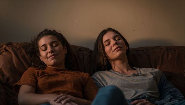 Two young women relaxing together on leather couch in warm soft light