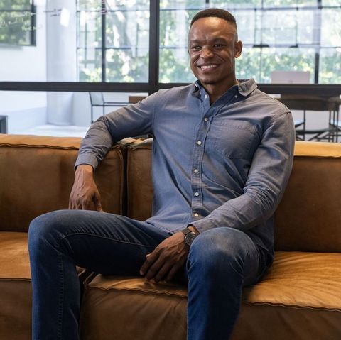 Smiling african american professional relaxing on leather sofa in modern office lounge
