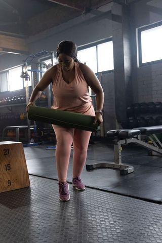 African american woman holding yoga mat preparing for strength workout in industrial gym