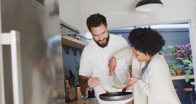 This image captures a happy diverse couple enjoying a moment together while cooking breakfast in a modern kitchen. They are smiling, sharing responsibilities, and showing love and inclusivity. The scene communicates togetherness, joy in daily routines, and a contemporary domestic atmosphere. This photo is perfect for promoting healthy relationships, lifestyle blogs, cooking websites, kitchen appliance promotions, or any content highlighting inclusivity and domestic bliss.