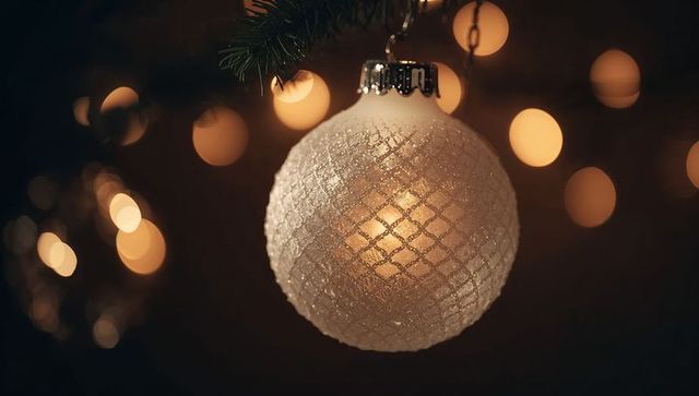 Frosted white christmas bauble hanging with warm bokeh glow and glitter crosshatch