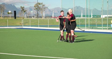 Diverse male field hockey players celebrating scores outdoors