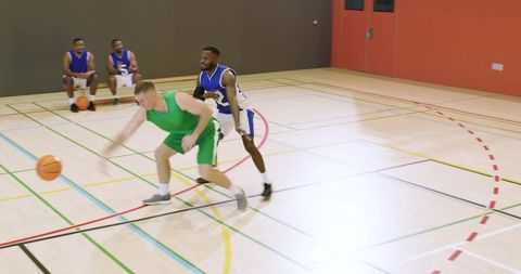 Green jersey dribbling while blue defender recovering during indoor basketball game