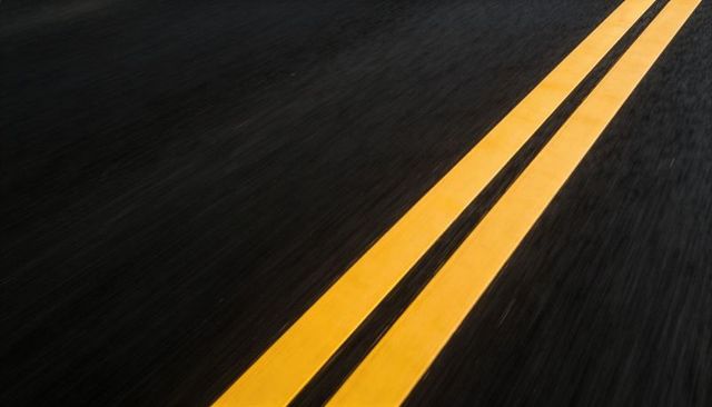 Diagonal double yellow centerline cutting through black asphalt texture with copy space