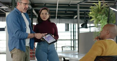 Multicultural team collaborating over tablet showing purple bar chart in modern loft office