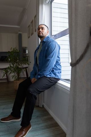 Contemplative african american man sitting on windowsill in modern living room interior