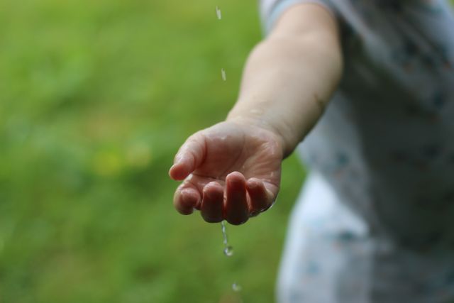 Child reaching out to touch raindrop in outdoor environment, symbolizing innocence and curiosity. Ideal for environmental, educational, and lifestyle contexts, or promoting connection with nature.