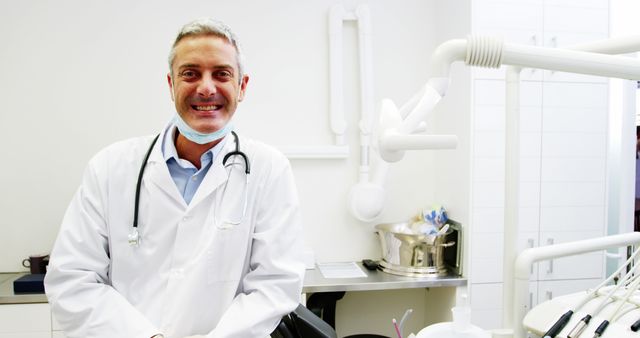 Smiling dentist in dental clinic, surrounded by tools and equipment. Useful for content on healthcare, dental professionals, medical services, oral care, and clinical environments.