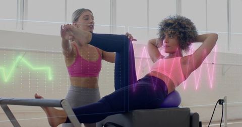 Woman performing pilates reformer crunch with trainer assisting on fitness ball