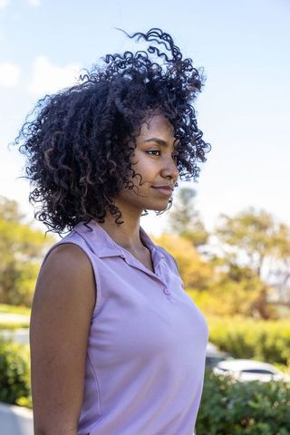 Sunlit african american woman with natural curly hair wearing lavender polo in park
