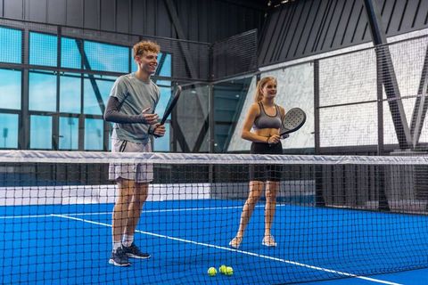 Young teammates playing padel on vibrant indoor blue court smiling and holding rackets