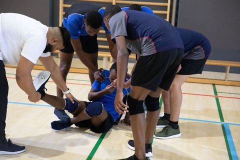 Basketball teammates helping injured player on gym floor showing teamwork and support