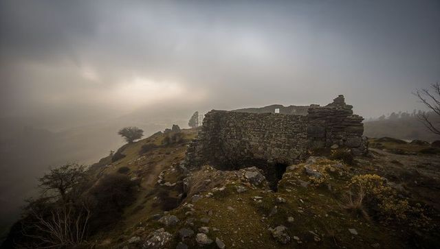Ruined dry-stone wall dominating foggy moorland hilltop, weathered stone remnant at dawn