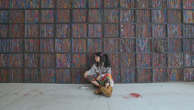 Woman sitting on floor against colorful cubby grid wall wearing patterned clothes and boots