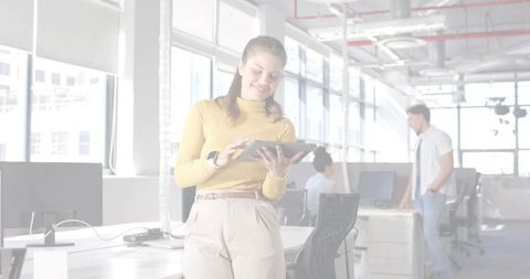 Young professional tapping tablet while leaning on desk in bright open-plan office