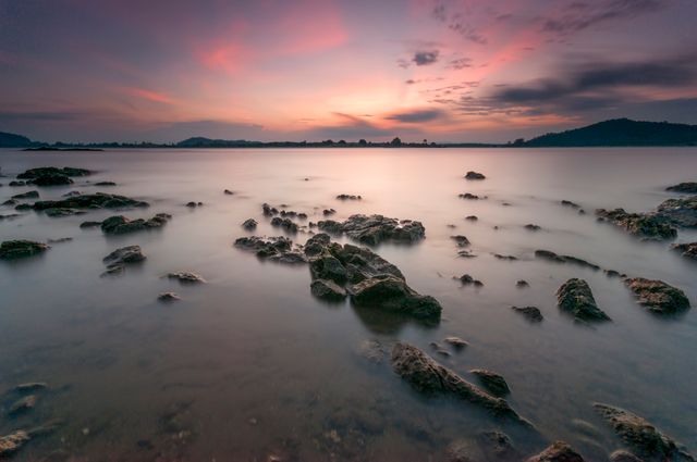 Twilight sky casting beautiful pink and purple hues above a still, rocky seashore. Ideal for use in travel brochures, nature posters, lifestyle blogs, or as a calming screensaver.