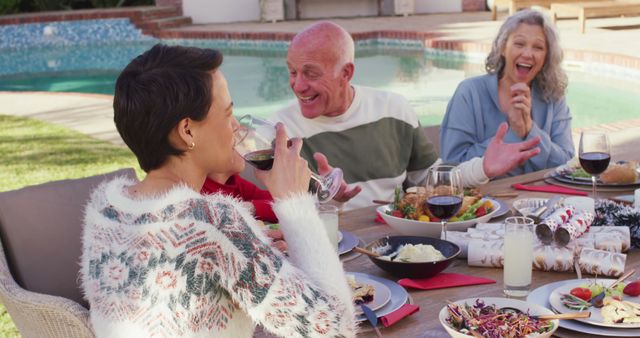 Family members sitting around a table by a swimming pool enjoying a meal together. Everyone is engaged in lively conversation and there is a joyful and relaxed atmosphere. Perfect for use in advertisements, blogs, or articles focused on family gatherings, outdoor dining, or leisure activities in summer.