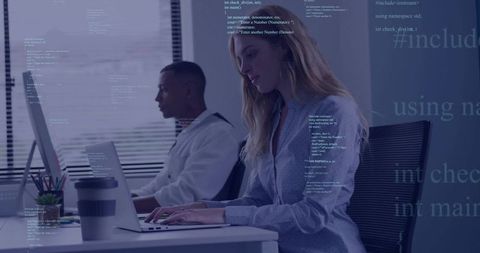 Typing woman working on laptop in modern office with coffee cup and colleague coding
