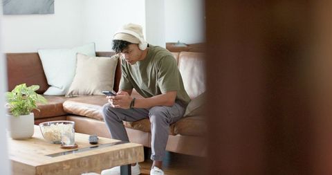 African american man listening with headphones using smartphone on cozy living room sofa