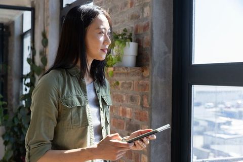 Asian Woman with Tablet Gazing Outside Urban Loft Window