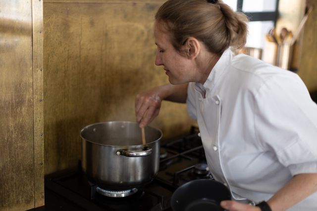 Caucasian female chef stirring cooking water in a pot. professional chef working in restaurant kitchen.