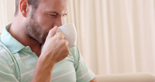 Man enjoying coffee in casual setting, perfect for lifestyle, relaxation, or beverage advertisements. Ideal for use in promotions for home products, morning routines, or wellness themes.