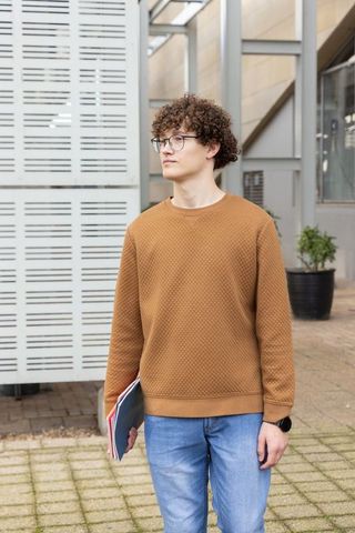 Curly-haired male student standing in urban campus courtyard holding notebooks and folders