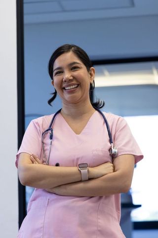 Smiling nurse standing with folded arms wearing pink scrubs and stethoscope in clinic