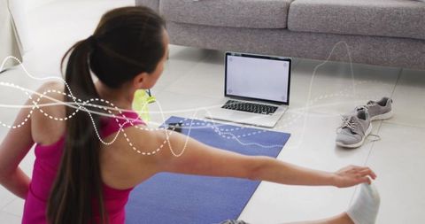 Woman stretching on yoga mat with laptop for home workout and mindfulness practice