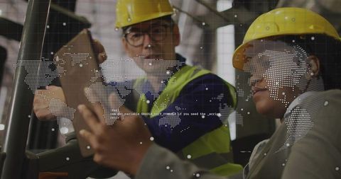 Asian man and woman reviewing tablets in warehouse with yellow hard hats and hi-vis vests