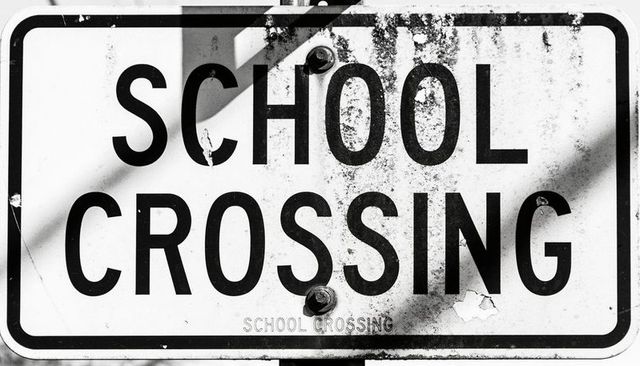 Weathered school crossing sign showing rust, peeling paint, bolts and shadows