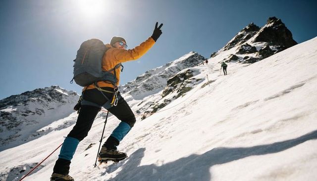 Mountaineer ascending snowy alpine slope with crampons and backpack giving victory sign