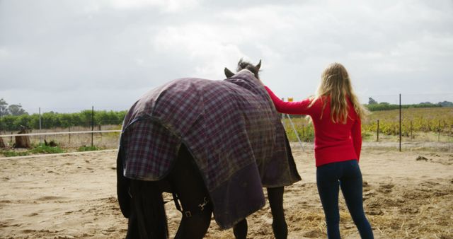 A woman standing beside a horse in a rural landscape. She comforts the horse by placing a hand on its back. The scene is set in a countryside field, evoking themes of companionship, nature, and rural life. This visual can be used for themes relating to animal welfare, farming, or human-animal relationships.