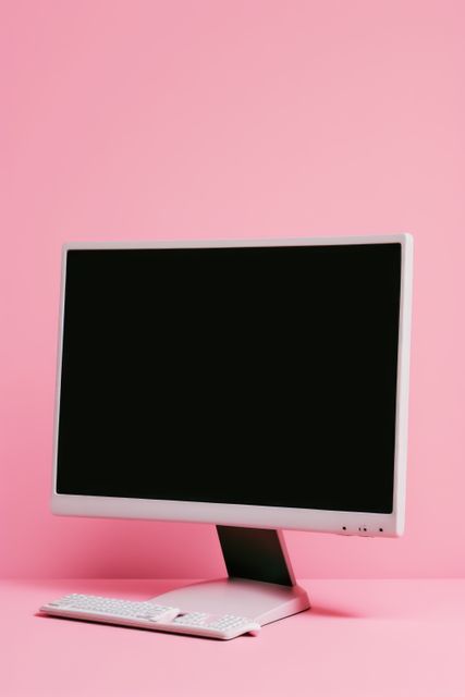 Modern desktop computer with monitor and keyboard posed on pink background, ideal for themes related to technology, modern workplace setups, minimalism, and feminine aesthetics.