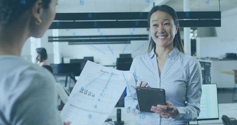 Korean businesswoman smiling presenting tablet during collaborative open-plan office meeting