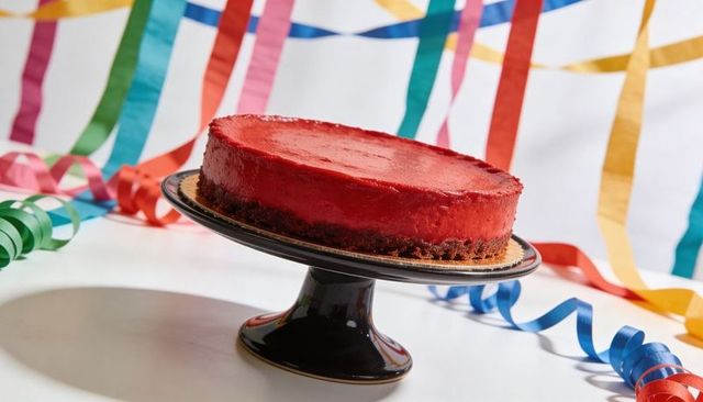 Red Glazed Cake Sitting on Black Pedestal with Colorful Party Streamers