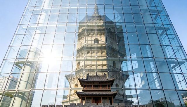 Historic stone pagoda reflecting in modern glass tower with wooden pavilion foreground