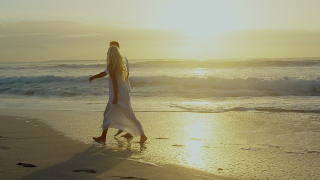 Young couple walking barefoot on a beach holding hands during sunset. Ideal for use in travel promotions, romantic getaway brochures, relationship advice articles, and lifestyle blogs focusing on relaxation and tranquility by the ocean.