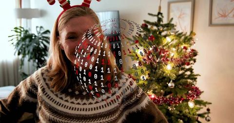 Smiling woman in knit sweater and antler headband celebrating holiday with digital code globe